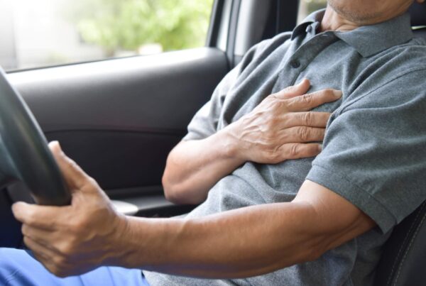 Older driver clutching his chest, experiencing chest pain after a car accident.