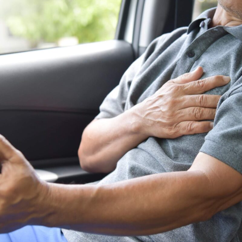 Older driver clutching his chest, experiencing chest pain after a car accident.